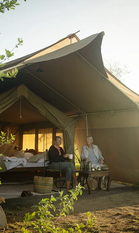 Canvas tent accommodation with guests relaxing on deck at dusk