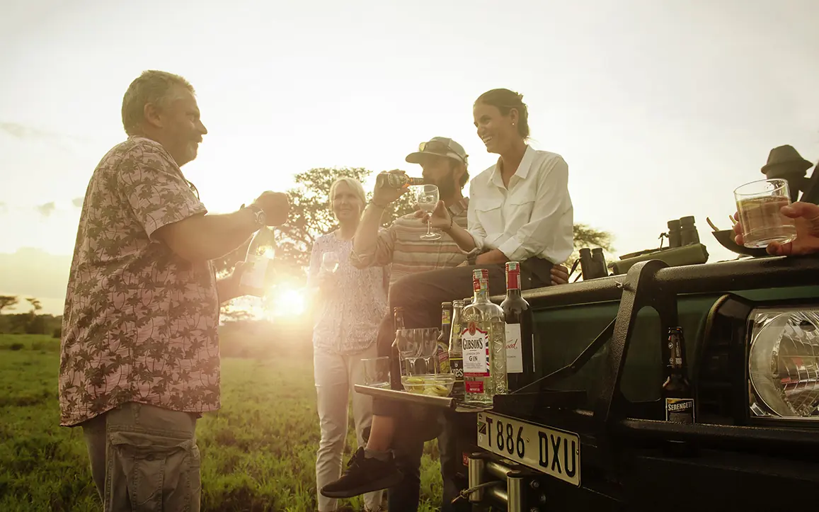 Guests gathered at vehicle during golden hour sunset, Pembazoni Camp, Serengeti National Park, Tanzania