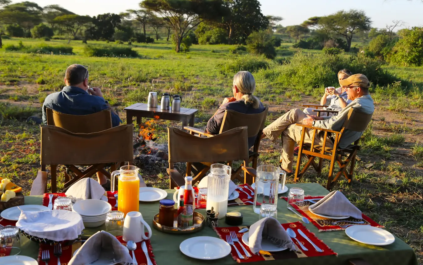 Guests dining outdoors at table in savanna landscape, Pembazoni Camp, Serengeti National Park, Tanzania