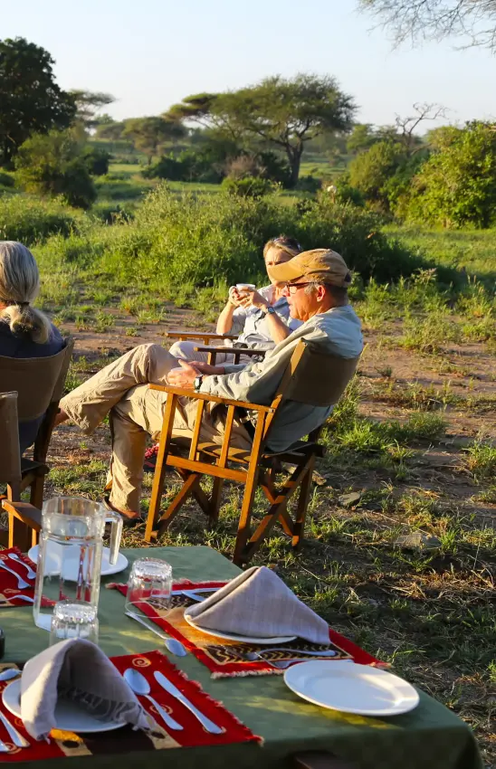 Guests dining outdoors at table in savanna landscape, Pembazoni Camp, Serengeti National Park, Tanzania