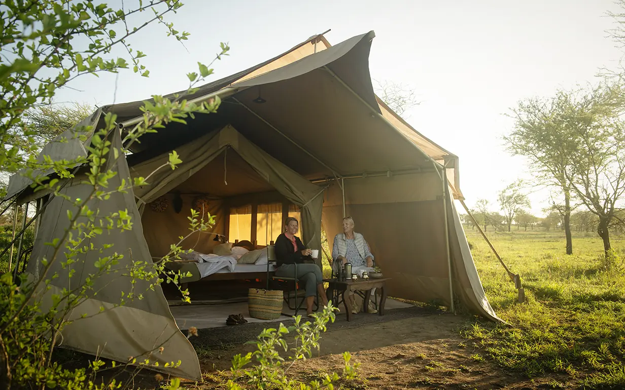Canvas tent accommodation with guests relaxing on deck at dusk, Pembazoni Camp, Serengeti National Park, Tanzania
