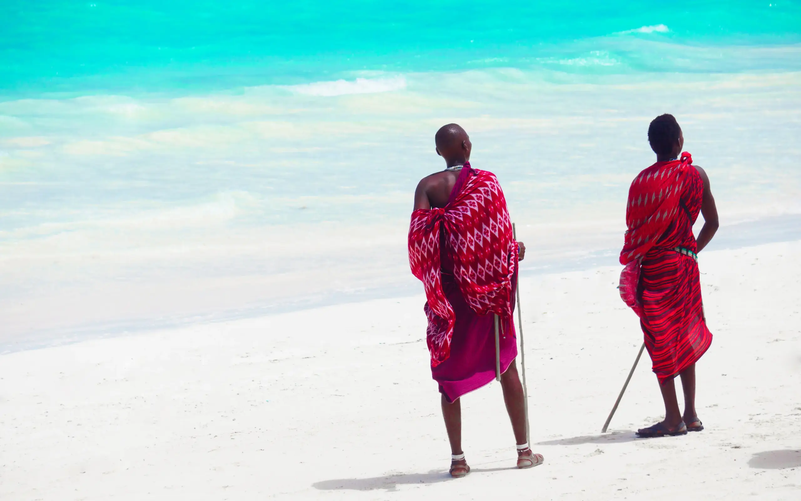 Two people in red traditional dress on white sand beach