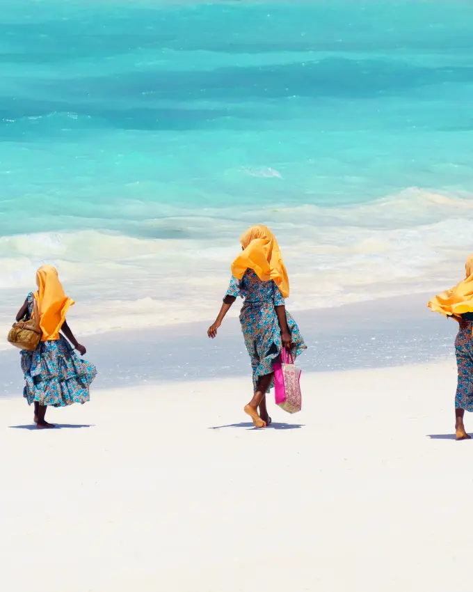 Three people in yellow headscarves walking on beach