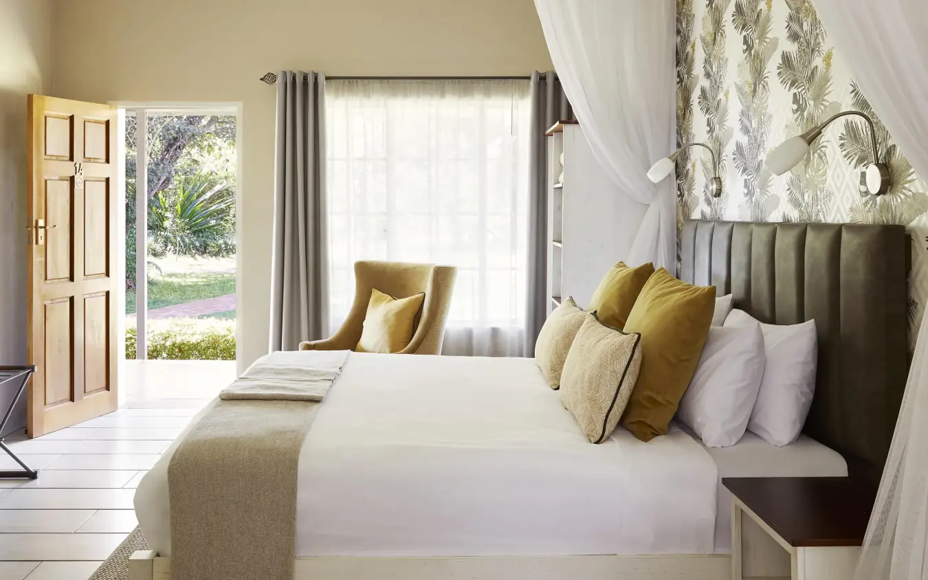 Bedroom with white bed, yellow pillows, and garden view, Pioneers Lodge, Victoria Falls, Zimbabwe