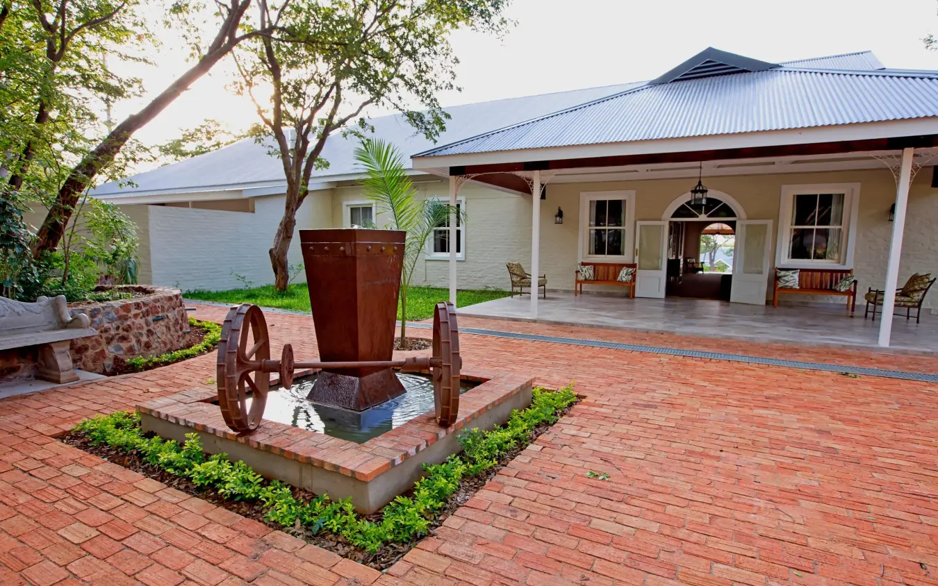 Cream brick lodge with covered porch and brick courtyard, Pioneers Lodge, Victoria Falls, Zimbabwe