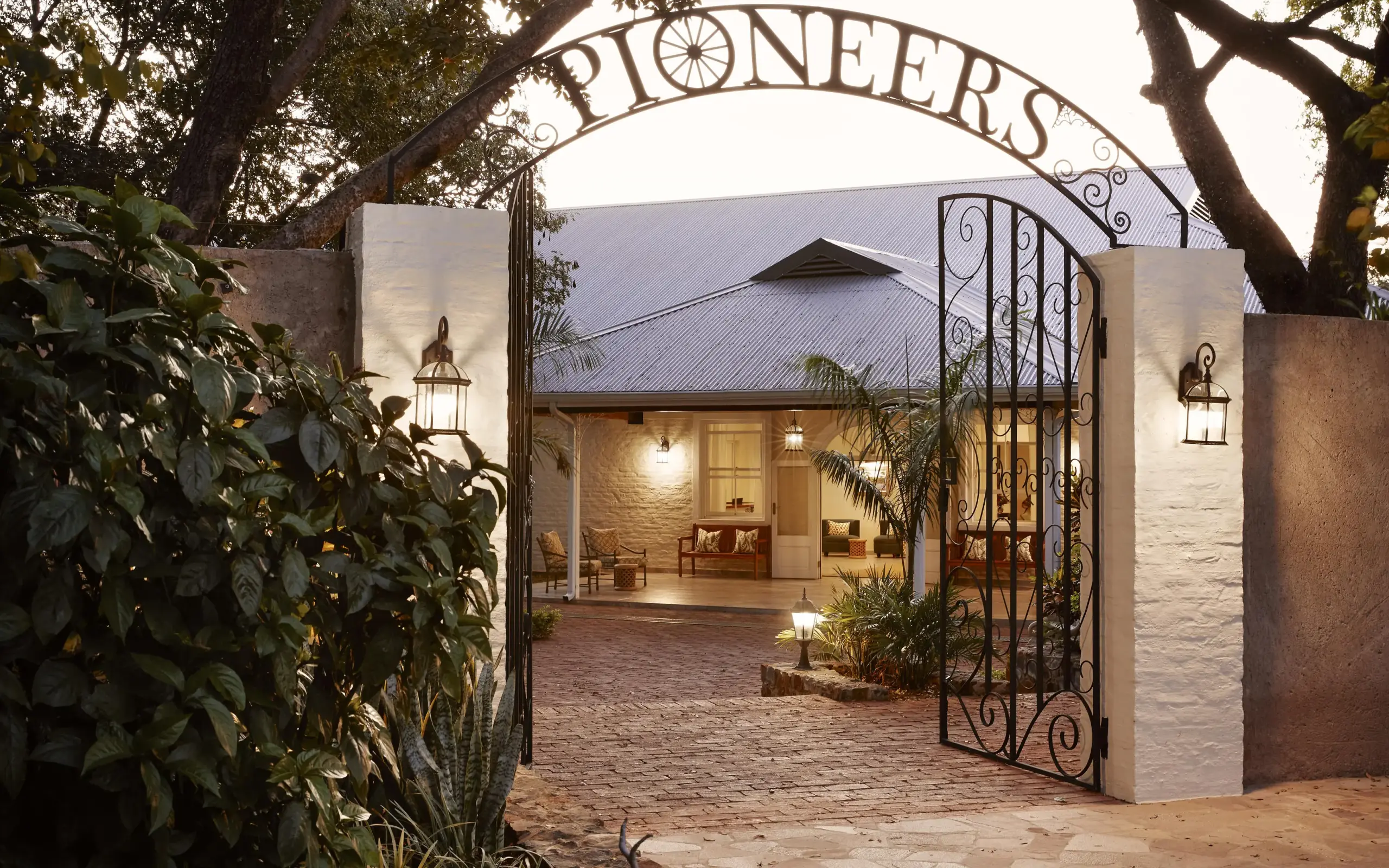 Illuminated entrance courtyard with decorative iron gate at dusk, Pioneers Lodge, Victoria Falls, Zimbabwe