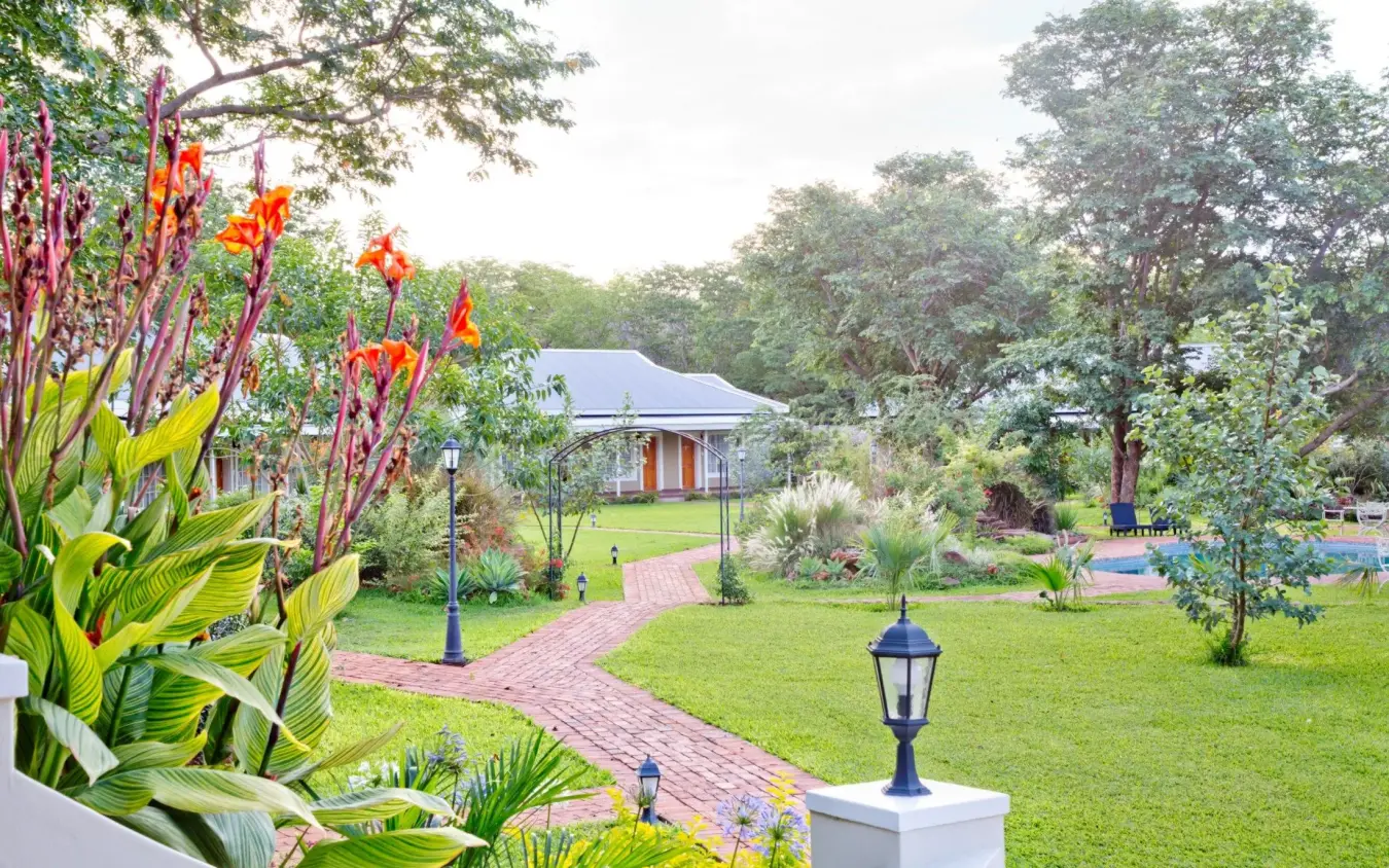 Manicured gardens with flowering plants leading to main lodge building, Pioneers Lodge, Victoria Falls, Zimbabwe