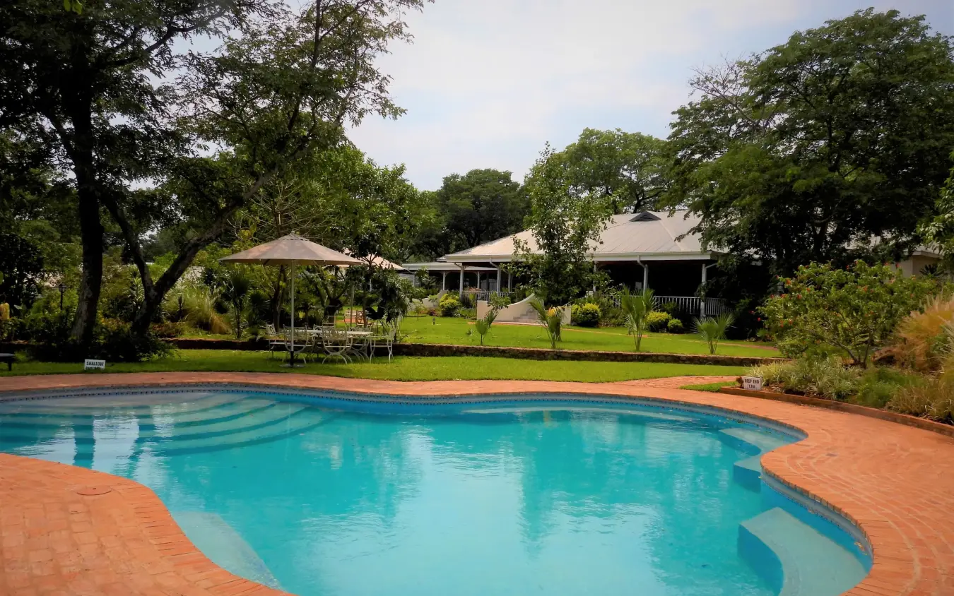 Curved swimming pool with terracotta deck and lodge buildings, Pioneers Lodge, Victoria Falls, Zimbabwe
