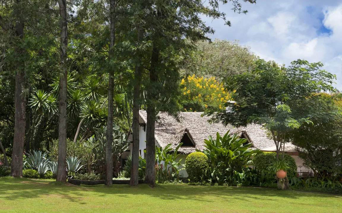 Colonial stone building with manicured lawn and mature trees, Plantation Lodge, Ngorongoro Crater, Tanzania