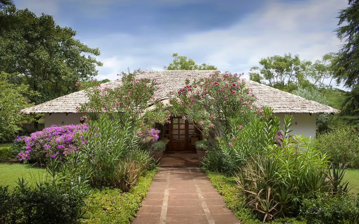 Thatched roof building with flowering plants and manicured gardens, Plantation Lodge, Ngorongoro Crater, Tanzania