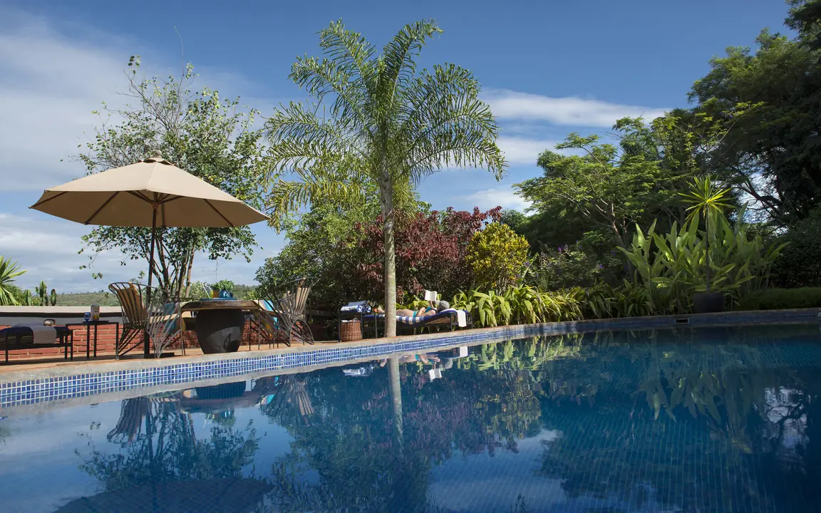 Resort swimming pool with umbrella and tropical gardens, Plantation Lodge, Ngorongoro Crater, Tanzania