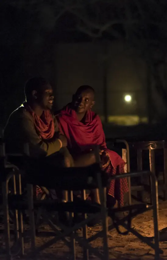 Two guests seated by firelight at night under starlit sky, Porini Amboseli Camp, Amboseli and Chyulu Hills, Kenya