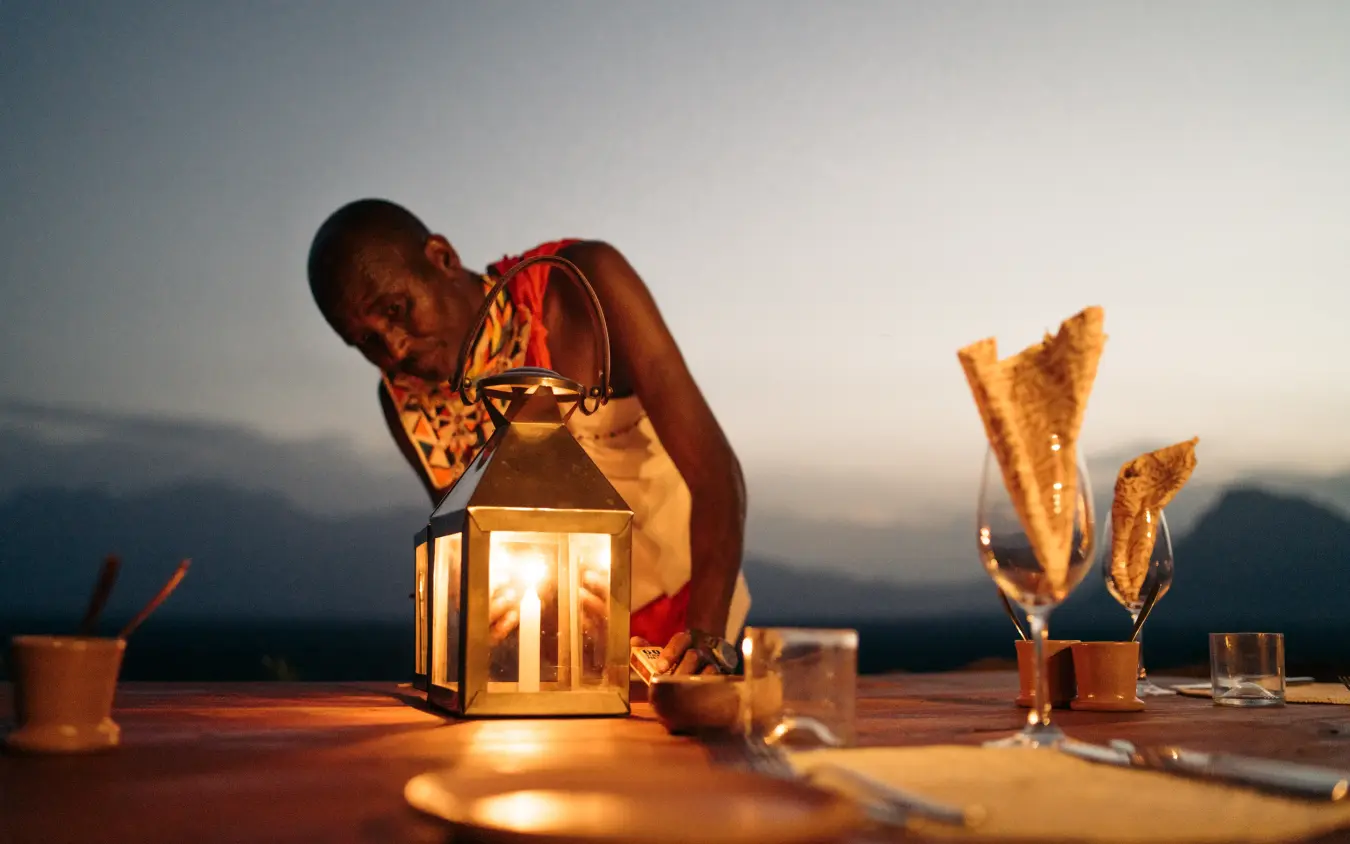 Person dining outdoors at sunset with lantern and appetizers, Reteti House, Northern Kenya, Kenya