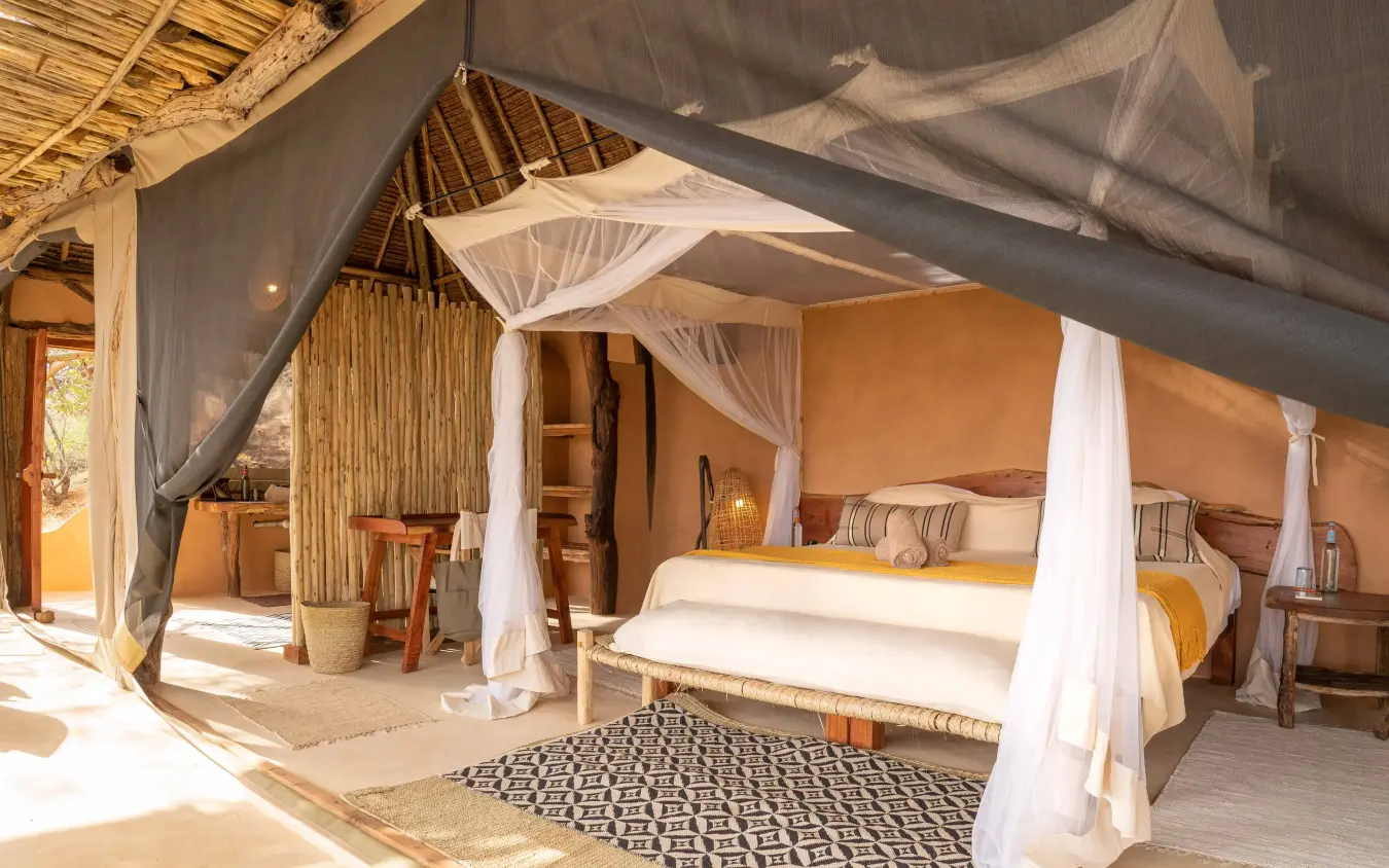 Spacious bedroom with white canopy bed and warm orange walls, Reteti House, Northern Kenya, Kenya