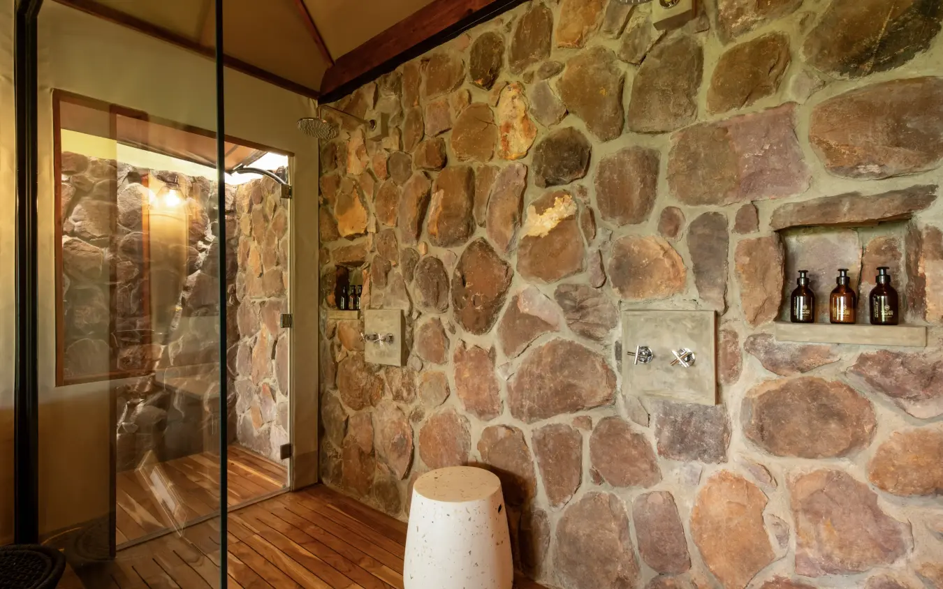 Stone bathroom with glass shower enclosure and wooden floors, The Retreats at Sayari Camp, Serengeti National Park, Tanzania