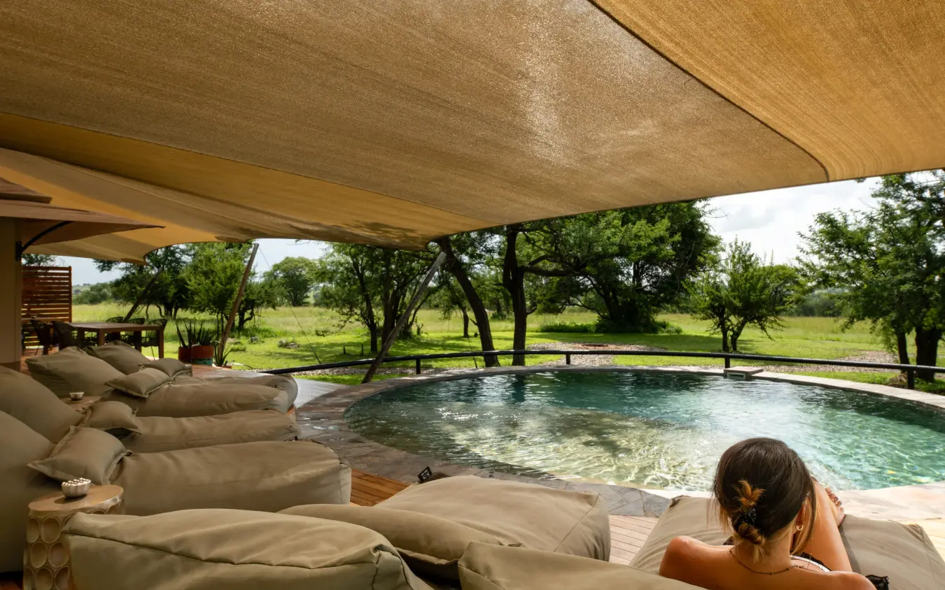 Guest relaxing by infinity pool overlooking savanna landscape, The Retreats at Sayari Camp, Serengeti National Park, Tanzania