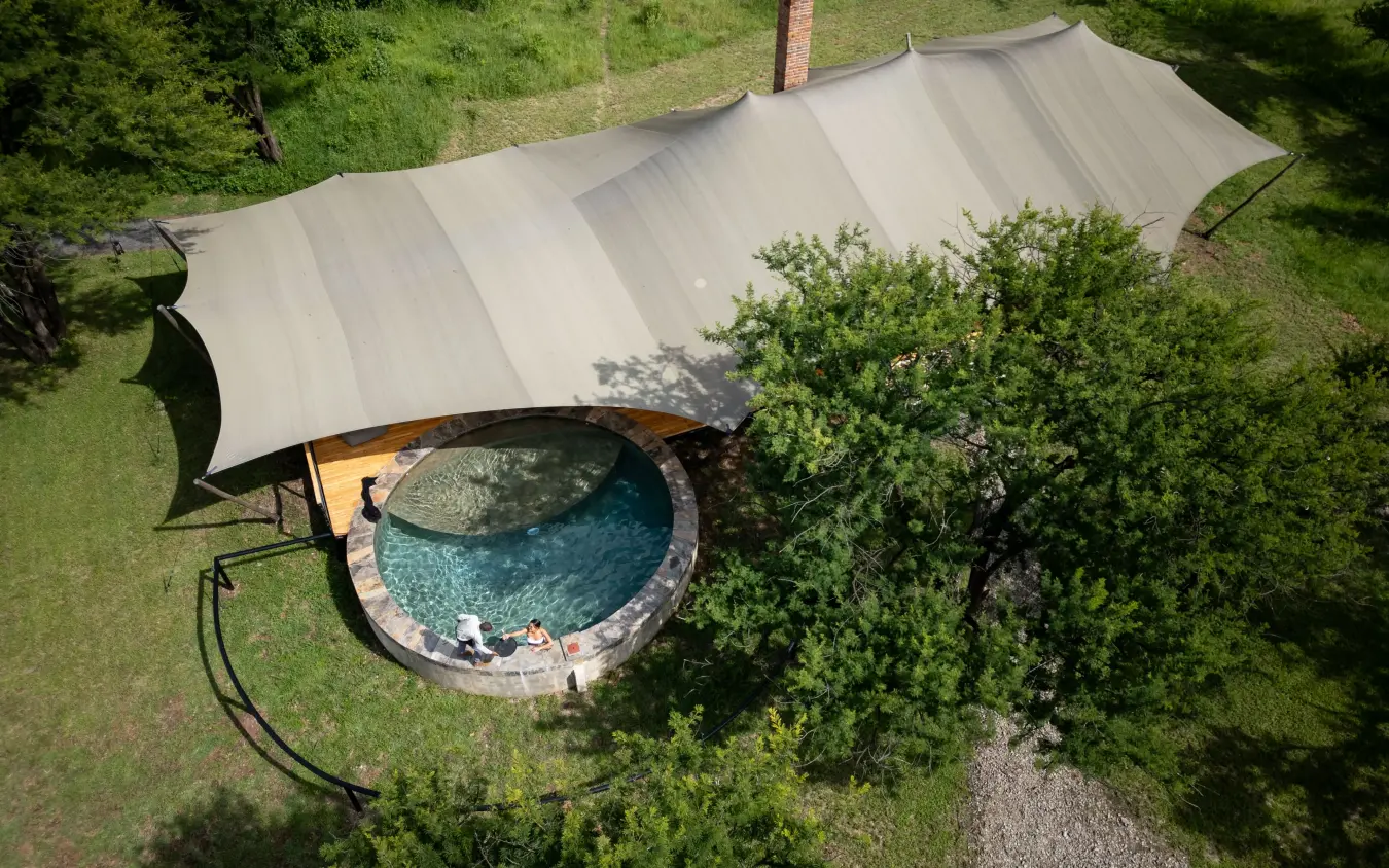 Aerial view of circular pool with shade structure and surrounding vegetation, The Retreats at Sayari Camp, Serengeti National Park, Tanzania