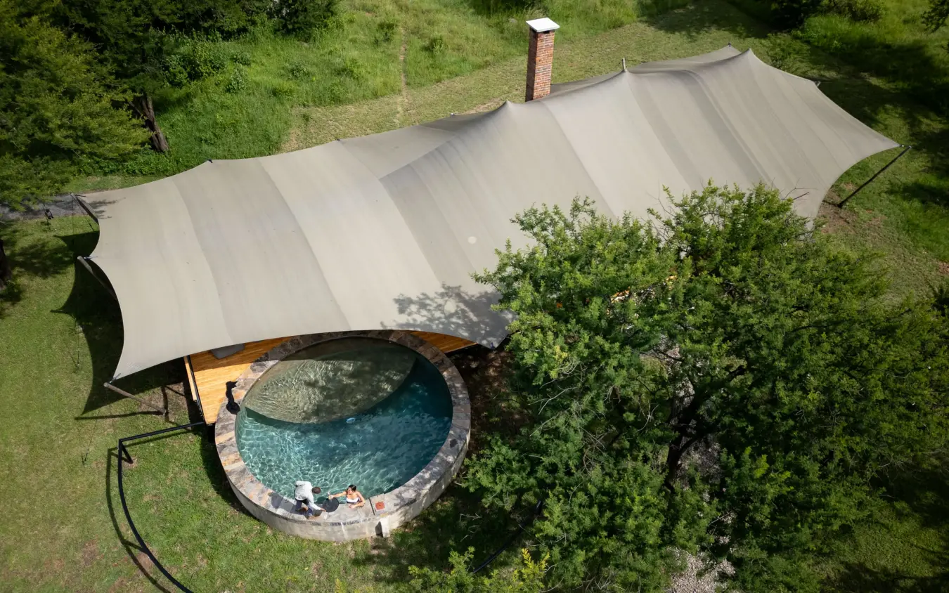 Circular pool with shade structure surrounded by green vegetation, The Retreats at Sayari Camp, Serengeti National Park, Tanzania