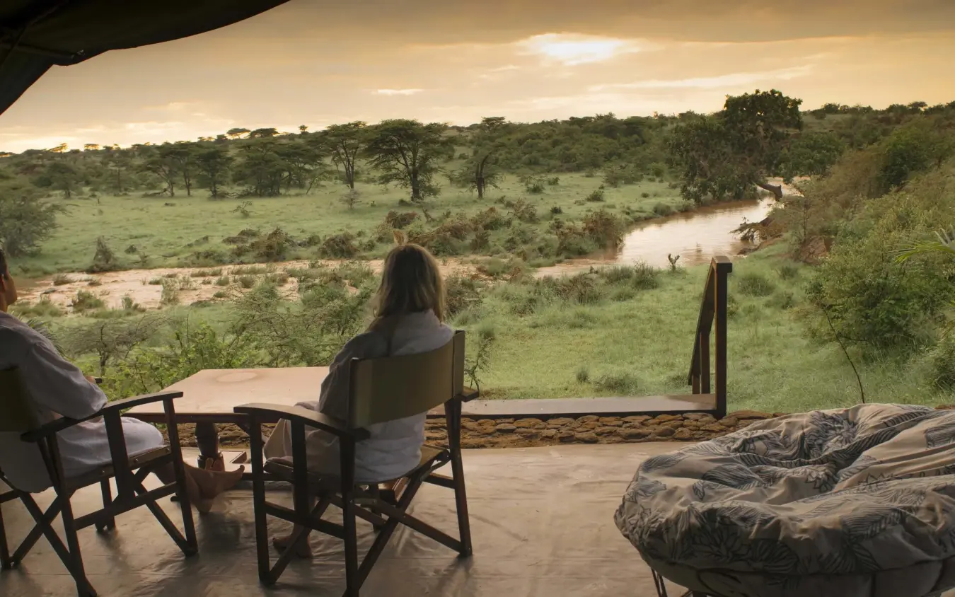 Two guests viewing river landscape from covered deck at sunset, Richard’s River Camp, Maasai Mara, Kenya