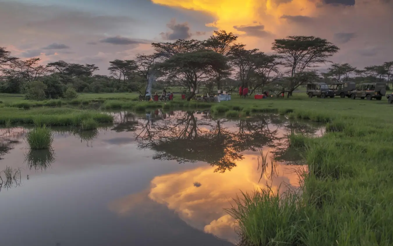 Sunset reflection over wetland with acacia trees and camp, Richard’s River Camp, Maasai Mara, Kenya