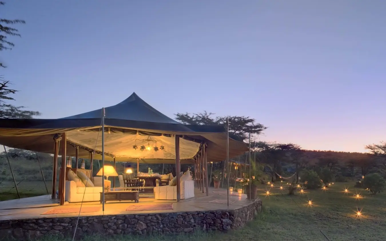 Illuminated safari lodge tent at dusk with landscape beyond, Richard’s River Camp, Maasai Mara, Kenya