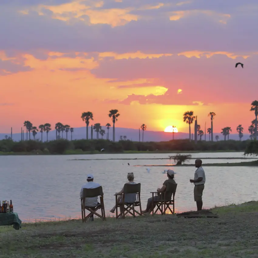 Guests watching sunset from riverbank chairs, Roho ya Selous, Nyerere National Park, Tanzania