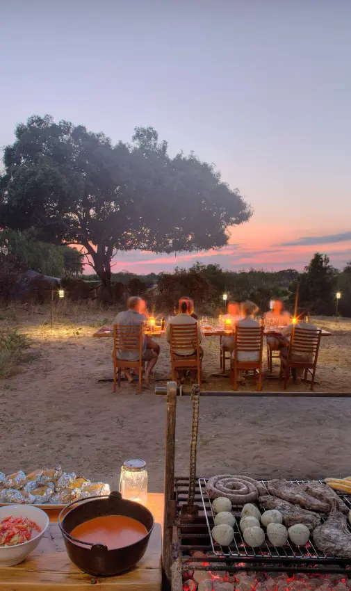 Outdoor dining setup at sunset with grilled food and chairs, Roho ya Selous, Nyerere National Park, Tanzania