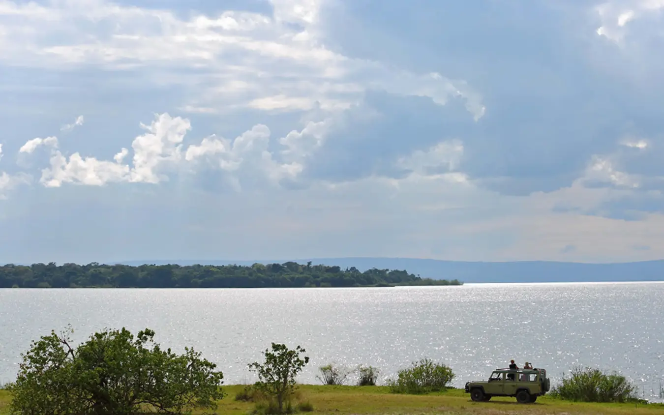 Safari vehicle parked on grassy shoreline overlooking calm water, Rubondo Island Camp, Rubondo Island, Tanzania