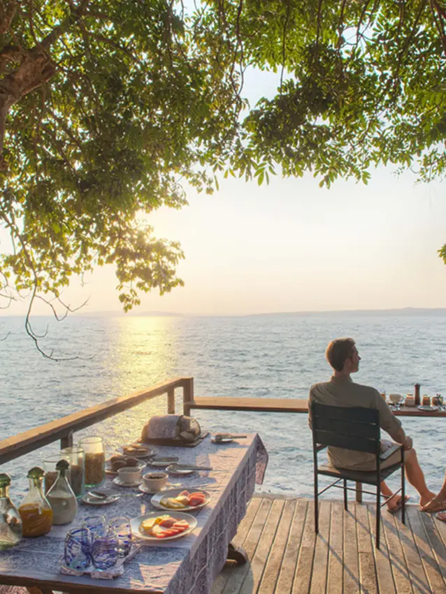 Couple dining on waterfront deck at sunset over lake, Rubondo Island Camp, Rubondo Island, Tanzania