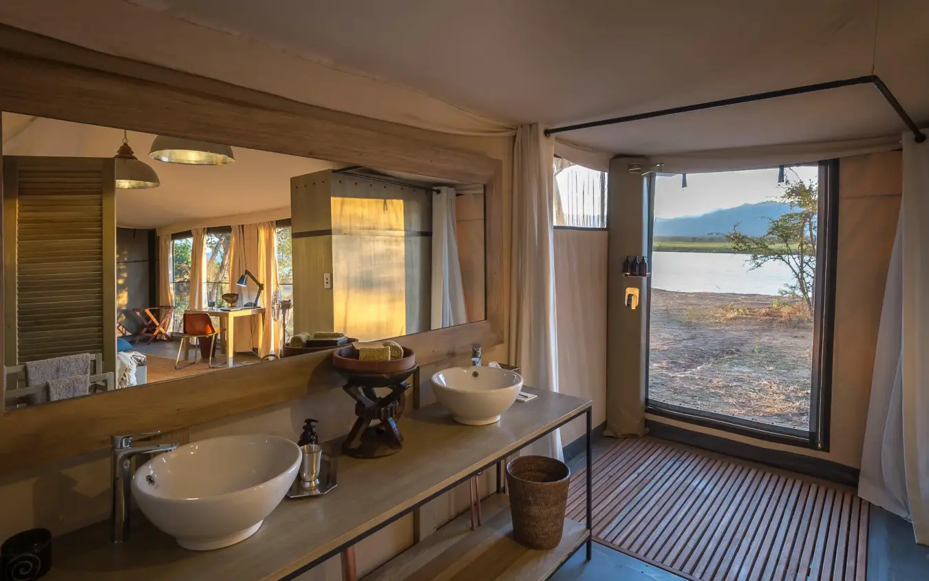 Luxury bathroom with dual sinks overlooking water and landscape, Ruckomechi Camp, Mana Pools, Zimbabwe