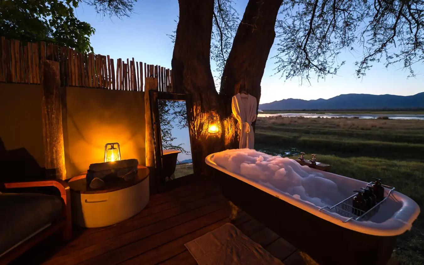 Outdoor bathtub on wooden deck overlooking savanna at dusk, Ruckomechi Camp, Mana Pools, Zimbabwe