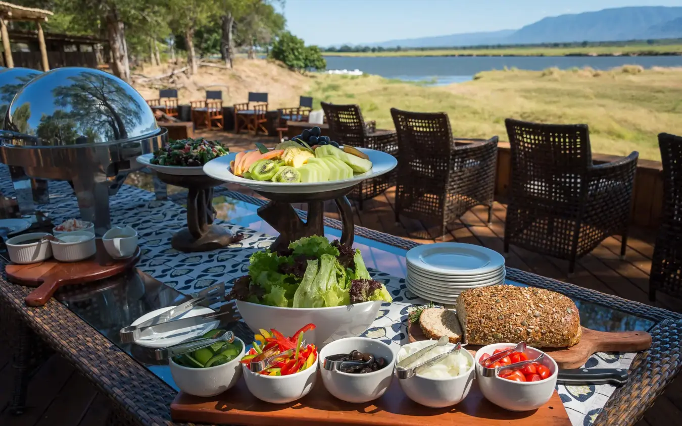 Outdoor lunch spread with fresh vegetables and lake view, Ruckomechi Camp, Mana Pools, Zimbabwe