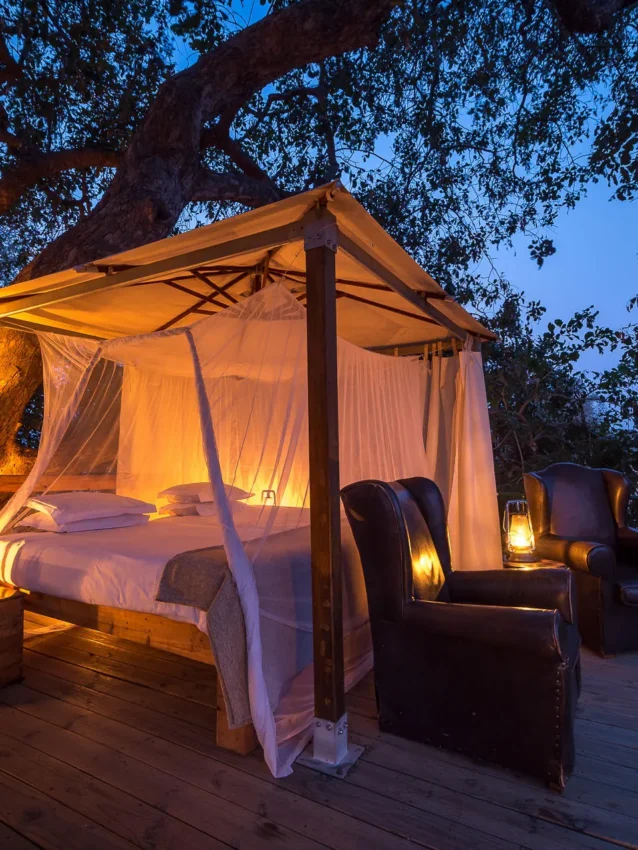 Illuminated canopy bed on wooden deck at dusk, Ruckomechi Camp, Mana Pools, Zimbabwe