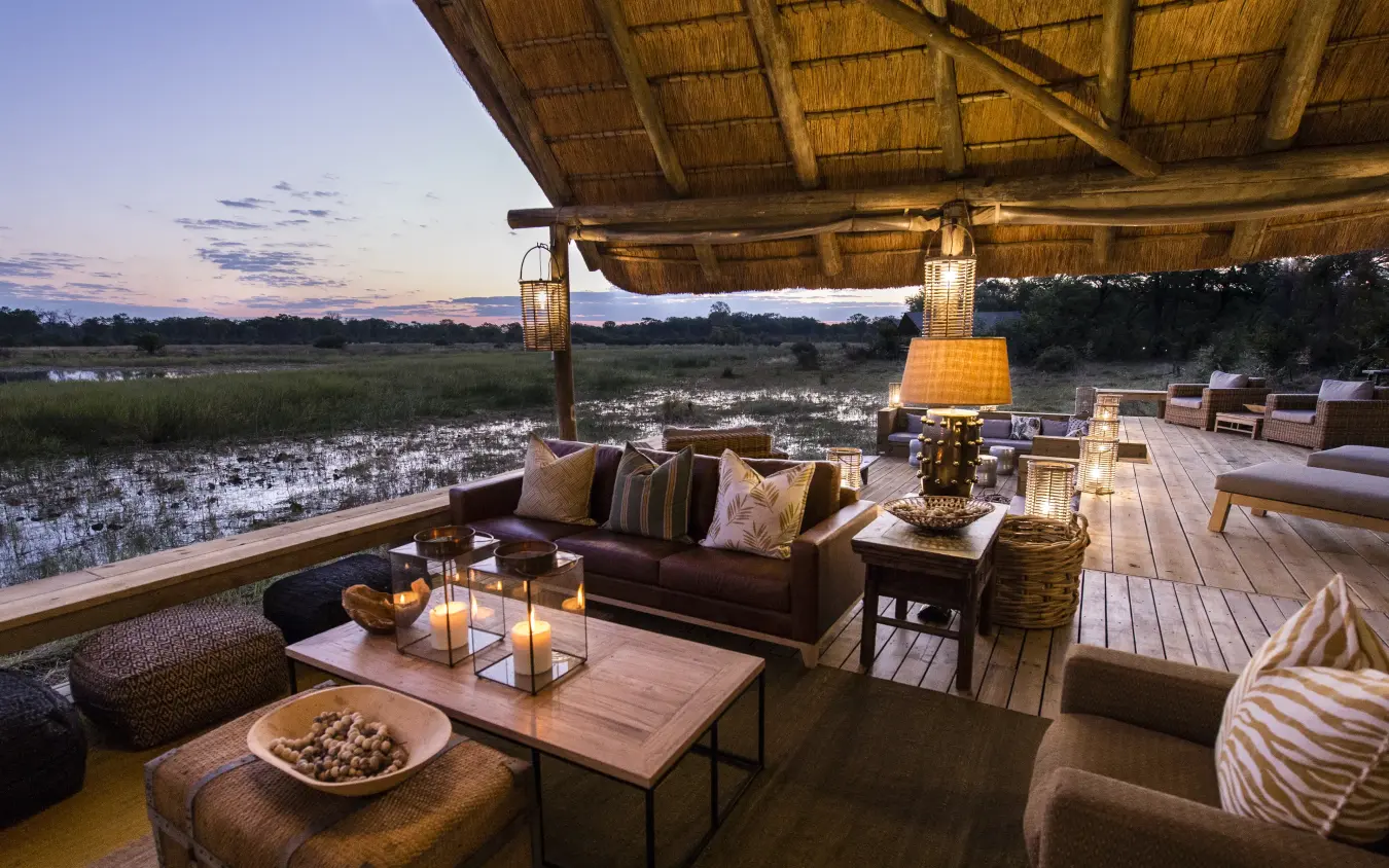 Thatched lounge overlooking wetlands at dusk with seating, Sable Alley, The Okavango Delta, Botswana