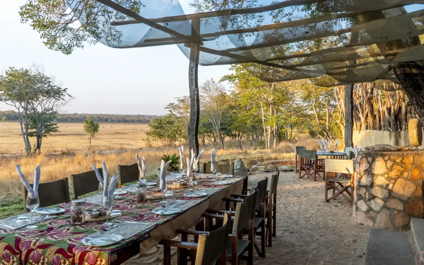 Outdoor dining setup under pergola with savanna landscape view, Sable Valley Lodge, Hwange National Park, Zimbabwe