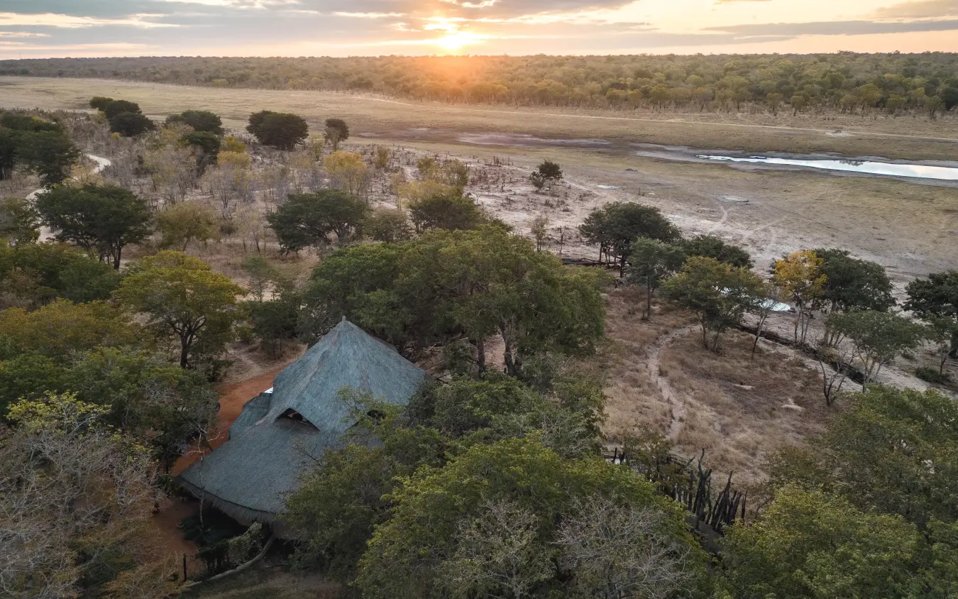 Thatched lodge nestled among trees overlooking floodplain at sunset, Sable Valley Lodge, Hwange National Park, Zimbabwe