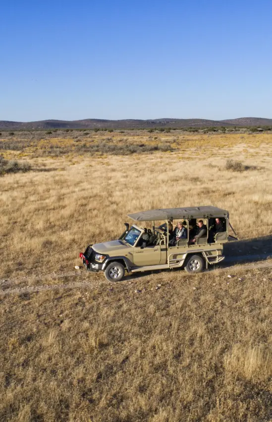Safari vehicle with passengers crossing open grassland plains, Safari House, Etosha National Park, Namibia
