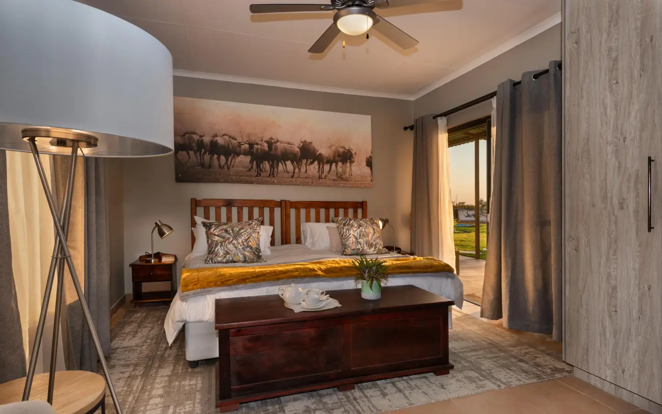 Spacious bedroom with wooden bed and safari artwork, Safari House, Etosha National Park, Namibia