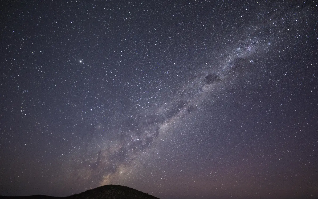 Milky Way galaxy stretching across night sky above dark hillside, Safari House, Etosha National Park, Namibia