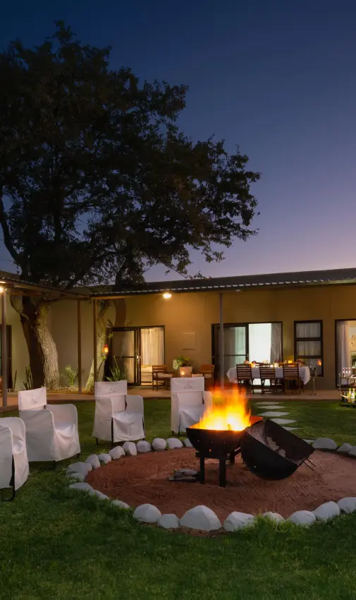 Courtyard with firepit, seating, and acacia tree at dusk, Safari House, Etosha National Park, Namibia