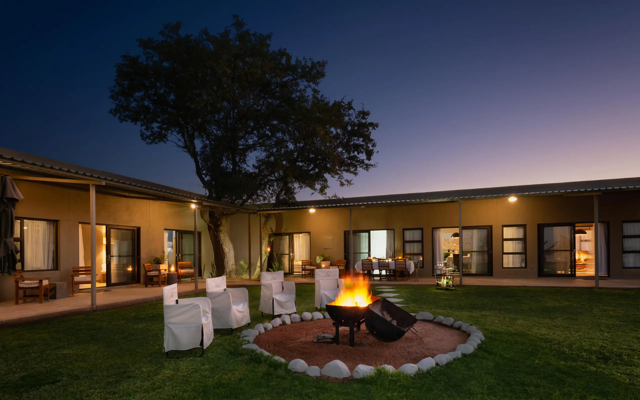Courtyard with firepit, seating, and acacia tree at dusk, Safari House, Etosha National Park, Namibia