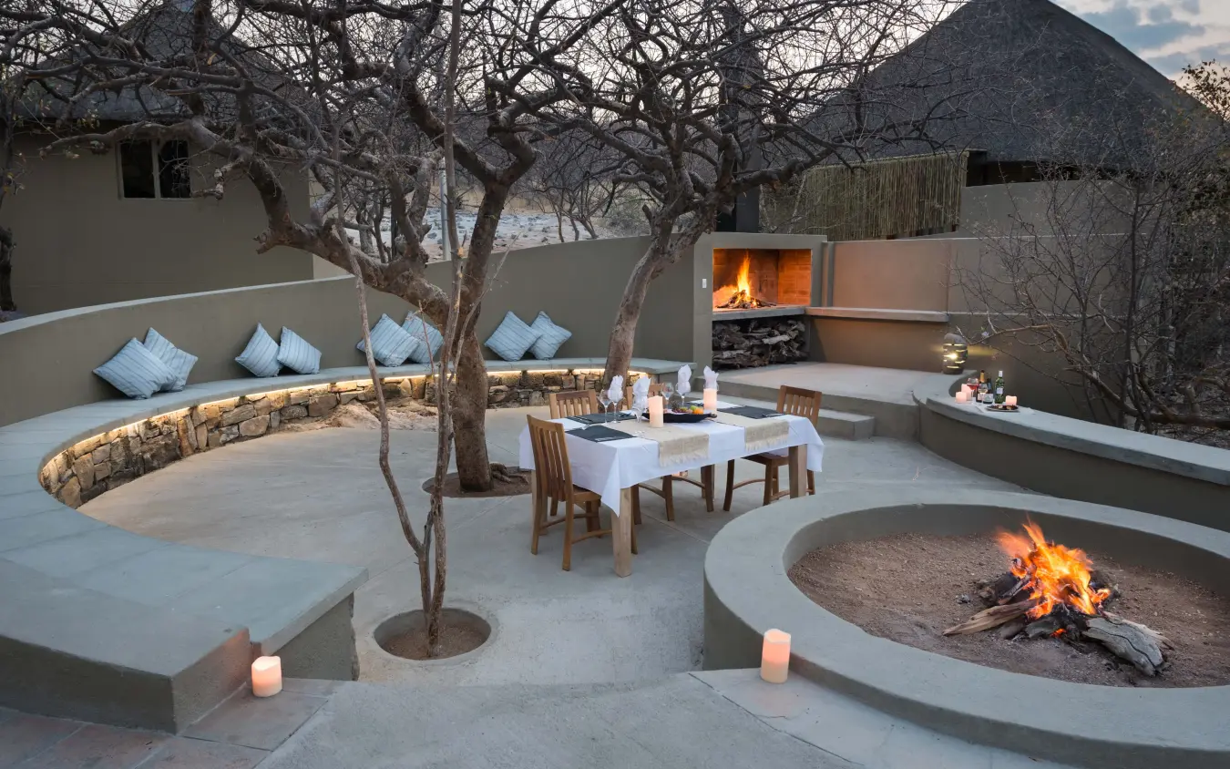Luxury outdoor lounge with firepit and dining area under bare trees, Safarihoek Lodge, Etosha National Park, Namibia