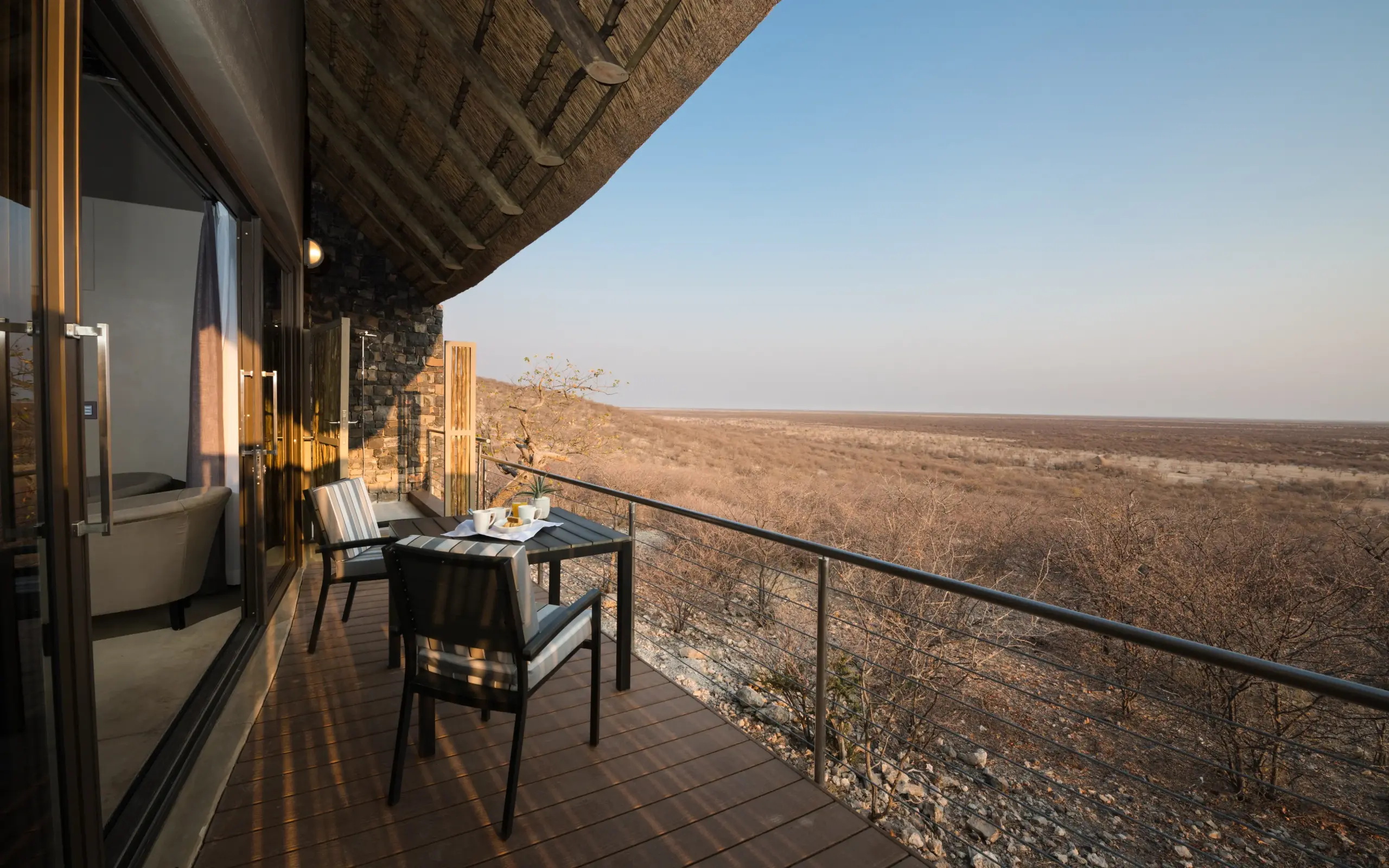 Luxury deck with dining furniture overlooking vast arid landscape at sunset, Safarihoek Lodge, Etosha National Park, Namibia