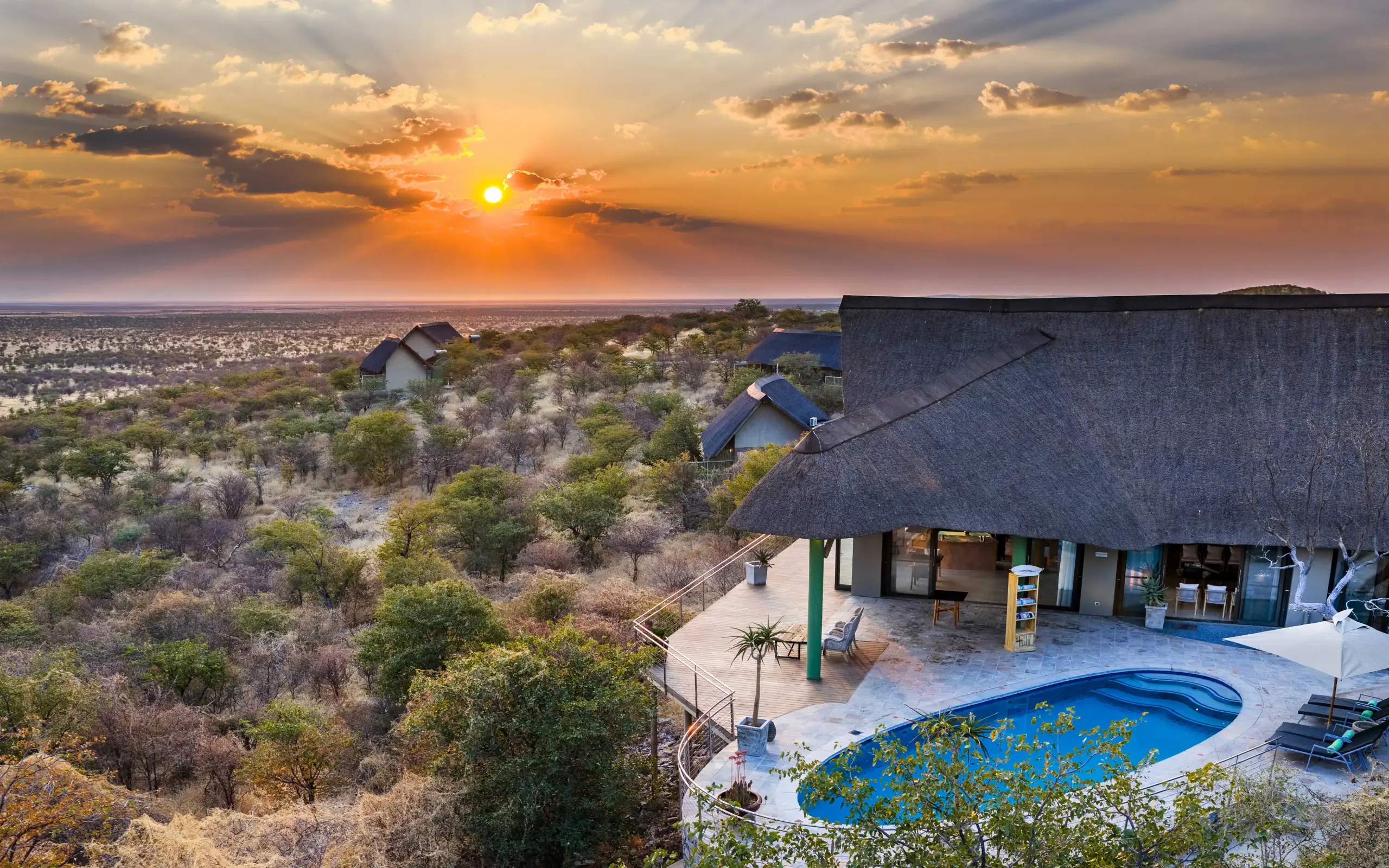 Luxury lodge with thatched roof and pool overlooking vast savanna landscape at sunset, Safarihoek Lodge, Etosha National Park, Namibia