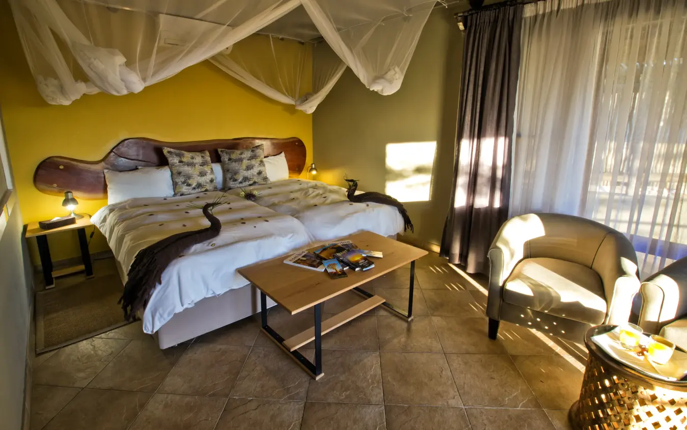 Luxury bedroom with canopy bed and yellow walls overlooking savanna landscape, Safarihoek Lodge, Etosha National Park, Namibia