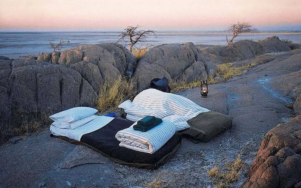 Bedding laid out on ground at sunset overlooking water, San Camp, Makgadikgadi Pans, Botswana