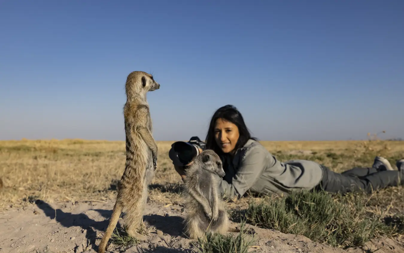 Photographer lying on ground photographing standing meerkat, San Camp, Makgadikgadi Pans, Botswana