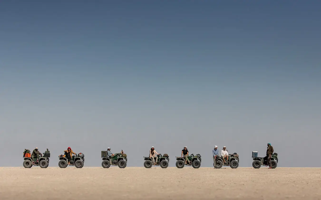 Line of quad bikers traversing flat desert landscape, San Camp, Makgadikgadi Pans, Botswana