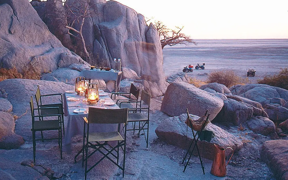 Outdoor dining setup on rocky beach at sunset, San Camp, Makgadikgadi Pans, Botswana