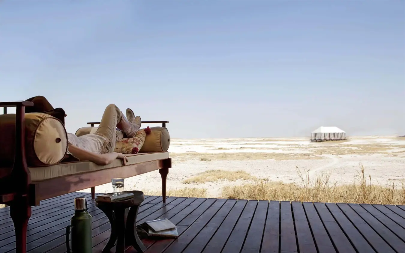 Guest relaxing on deck chair overlooking salt pan landscape, San Camp, Makgadikgadi Pans, Botswana